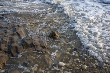 pebble stones on the sea beach, the rolling waves of the sea with foam