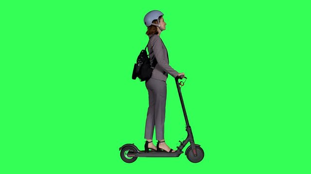 Riding an electric scooter happily, looking around and waving hello by a young businesswoman with a helmet over a green screen.
