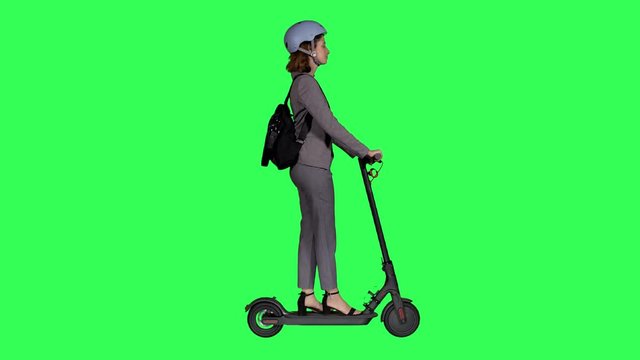 Riding an electric scooter to work by a young businesswoman wearing a helmet over a green screen,