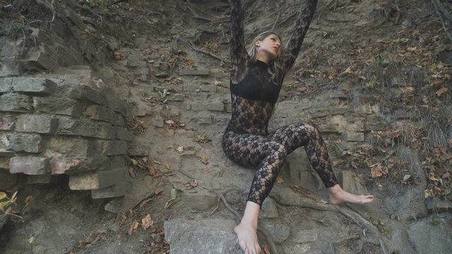 A beautiful blond girl in a body stocking tied with black ribbons to the roots is trying to free herself. Modern and fashion performance.