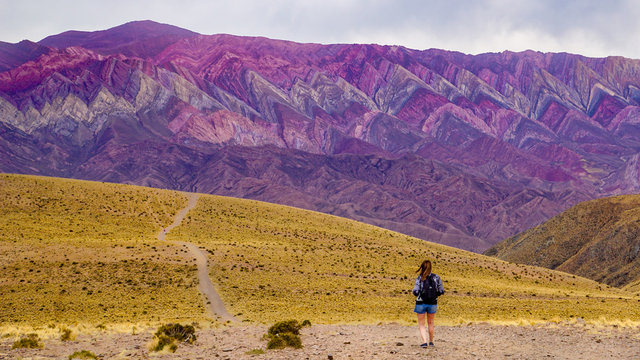 A young woman wearing shorts and a backpack approaches the Serranias de Hornocal (Cerro de Catorce Colores) mountains in the UNESCO-listed Quebrada de Humahuaca valley in north western Argentina