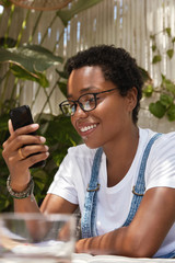 Rear view of content teenage girl with toothy smile, sends text message using new app on smart...