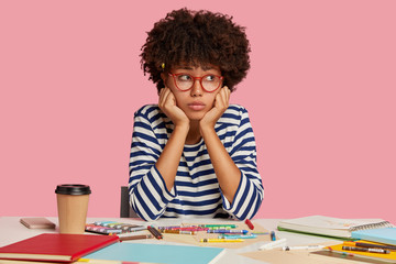 Sad cartoonist has no inspiration for drawing, holds chin and looks in displeasure aside, sits at...