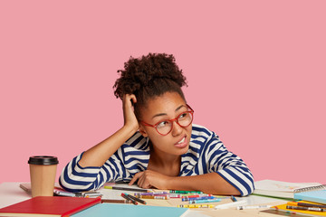 Horizontal shot of indignant woman scratches head, has curly dark hair, wears transparent glasses,...