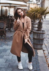 Fototapeta premium Sensual portrait of a young woman in brown coat. Woman posing outdoors on the street at overcast autumn day