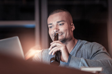 It is tasty. Attractive young man feeling happiness while being at work and holding bottle in left hand