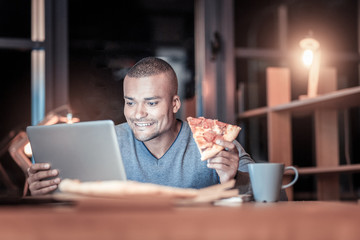 Time to eat. Relaxed brunette expressing positivity and having piece of pizza while looking at computer