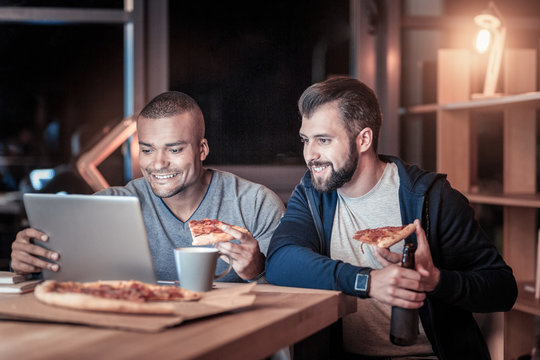 Day off. Positive delighted males sitting at workplace and looking at computer while watching video