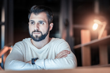 Need to think. Handsome programmer crossing arms while looking aside and siting at his workplace