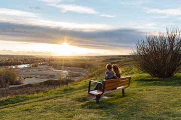 Fototapeta premium Woman and child sitting on a bench admiring the sunset