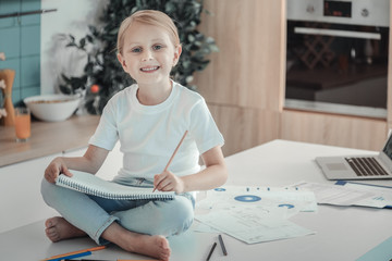 Young painter. Satisfied pleasant cute girl spending time in the kitchen sitting on the table near...