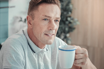 Catch the moment. Deep handsome satisfied man sitting in the empty room drinking tea and looking...