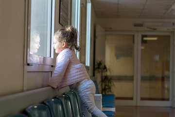 Little girl looking through a window from a hospital waiting room 