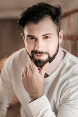 Fototapeta premium Feeling success. Attractive brunette keeping smile on his face and touching beard while being high spirited