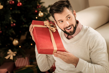 What is inside. Cheerful happy positive man holding a present and trying to guess what is inside...