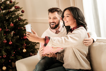 Our photograph. Joyful delighted positive couple sitting together and smiling while taking a selfie