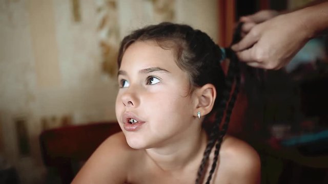 Mother is making of braids on little daughters head. Hairdresser is braiding the hair on young girl. Getting ready for school. mom and little girl caring family concept lifestyle