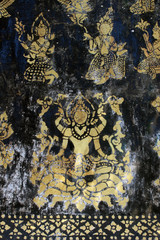Elements from an ancient aged decoration of gods or goddesses painted in gold on black on a wall at a Buddhist temple in south east Asia.
