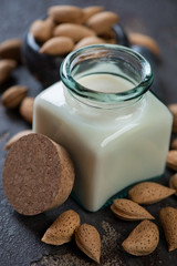 Close-up of a glass bottle with almond milk and unpeeled almond nuts, selective focus, vertical shot