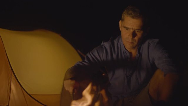 Portrait of a man poking the campfire at night