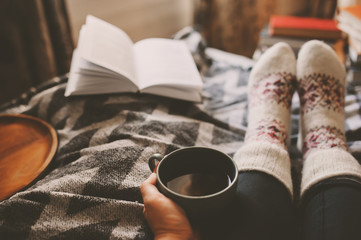 cozy winter day at home with cup of hot tea, book and warm socks. Spending weekend in bed, seasonal...