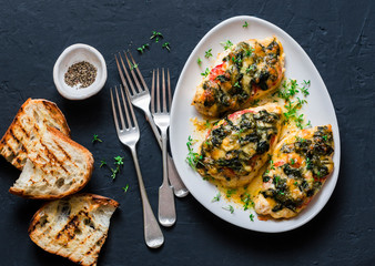 Baked chicken breast with tomatoes, spinach and mozzarella - delicious diet lunch in mediterranean style on a dark background, top view