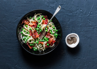 Spaghetti with bacon and creamy green peas on a dark background, top view