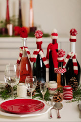 Merry Christmas and Happy New Year! Тable setting holiday knitted decor - Santa Claus knitted hats on the bottle with wine, candles in candlesticks in knitted decor.