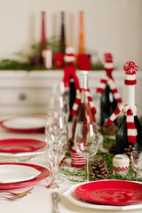 Merry Christmas and Happy New Year! Тable setting holiday knitted decor - Santa Claus knitted hats on the bottle with wine, candles in candlesticks in knitted decor.