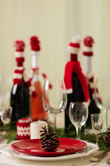 Merry Christmas and Happy New Year! Тable setting holiday knitted decor - Santa Claus knitted hats on the bottle with wine, candles in candlesticks in knitted decor.