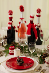 Merry Christmas and Happy New Year! Тable setting holiday knitted decor - Santa Claus knitted hats on the bottle with wine, candles in candlesticks in knitted decor.