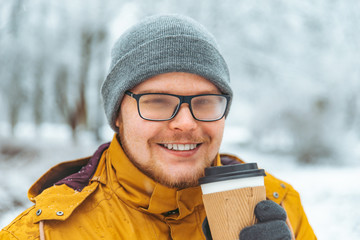 man drinking coffee to go outside in snowed winter day. glasses is misted