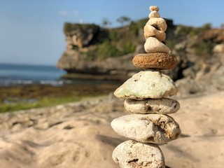 Different sized sand stones piled on top of each other as to keep balance without tumbling down, on the beach with sea in the background in the afternoon sun