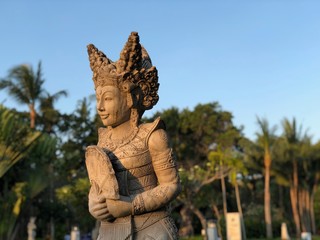 Female balinese dancer statue out of stone in Nusa dua Bali at sunset in late afternoon with palm trees in the background