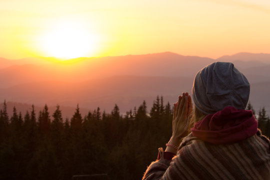 Unknown woman praying on sunrise in forest mountains. Meditation and spiritual practice concept. Praying hands. Yoga lifestyle. Morning dusk in mountains and praying girl. Space and vastness of nature