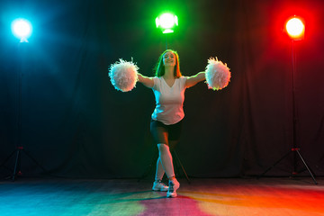 Dancing, sport, beautiful and people concept - young cheerleader girl in darkness show pom poms and...