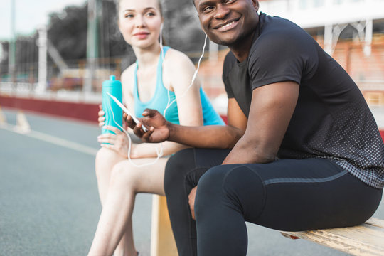 Group of athletes sitting on the bench and resting after hard street workout session. Man and woman doing urban sport. rest after sports, listen to music, drink water