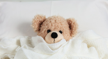 Cute teddy covered with a warm blanket, laying in bed