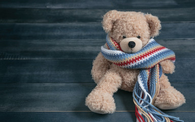Obraz premium Cute teddy bear with colorful scarf sitting on blue wooden background