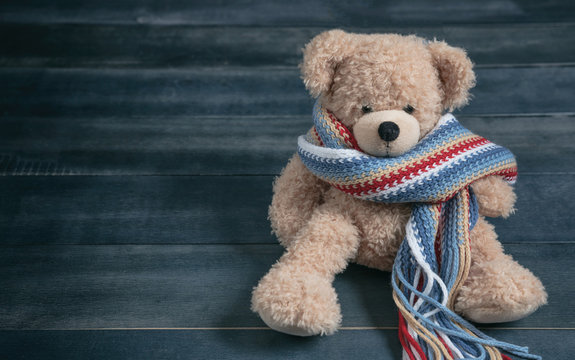 Naklejki Cute teddy bear with colorful scarf sitting on blue wooden background