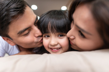 Asian Parents kissing their little daughter on both cheeks.