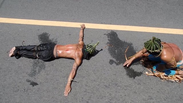 Unidentifiable maskedk penitent prone and lie prostrate on asphalt pavement beaten with bamboo stick imitating Christ&rsquo;s sufferings before crucifixion during Lenten week