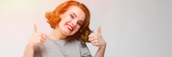 Charming young girl in a gray T-shirt on a gray background. Girl showing class sign