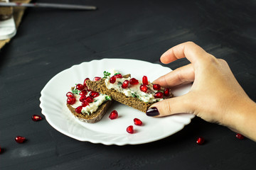sandwich with cheese, greens and pomegranate berries in a female hand