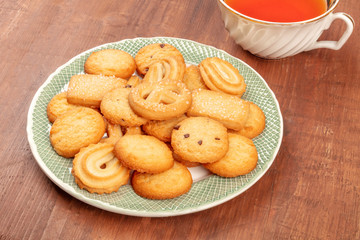 A photo of Danish butter cookies with a vintage tea cup on a dark rustic wooden background with copy space