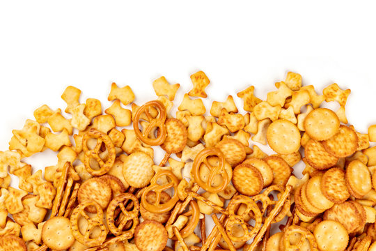 Many salty crackers, sticks, pretzels, and goldfishes, shot from above on a white background with copy space. Party snacks mix with a place for text