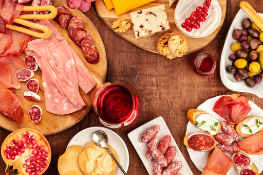 Charcuterie Tasting. A photo of many different sausages and hams, cold cuts, and a cheese platter, shot from the top on a rustic background with a glass of red wine, olives and copy space