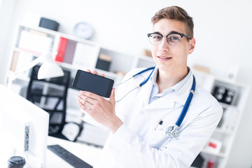 A young man in a white robe standing in the office and holding a phone.