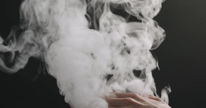 Slow motion closeup vapor rises through man hand from bottom on black background