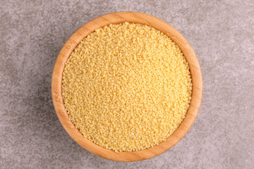 Raw couscous grain in wooden bowl on gray marble background